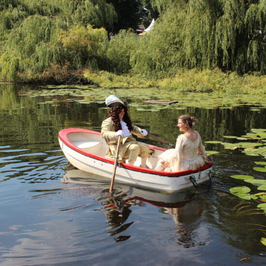 Zwei Tänzer in ihren Kostümen in einem kleinen Boot auf einem Teich